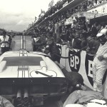 Carroll Shelby (center far right) confers with Ken Miles (black helmet) & Denis Holme (white helmet) during a routine pit stop